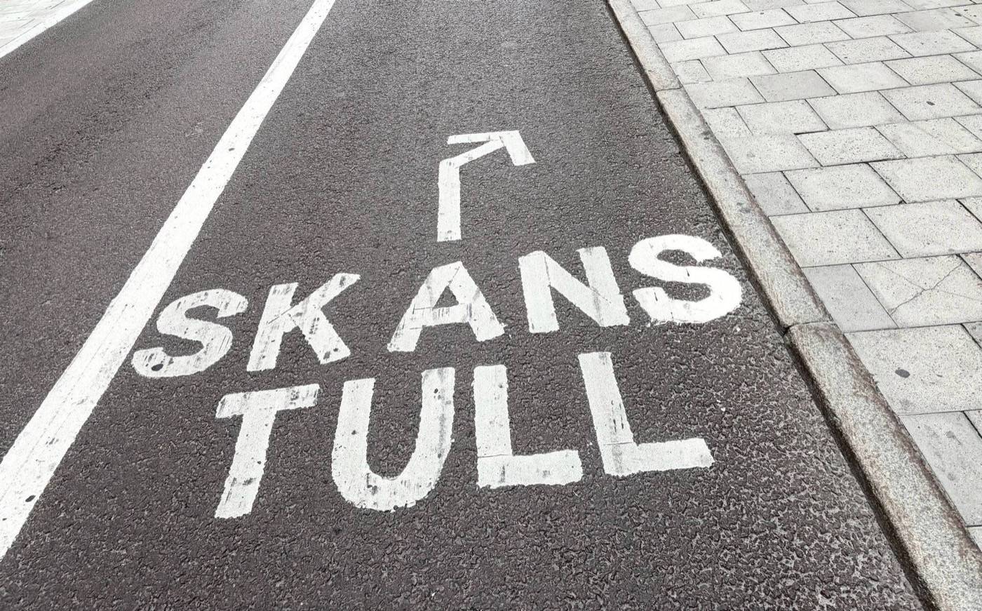 Vägmarkering på cykelbanan vid Skanstull: ordet Skanstull i vita versaler och en pil som visar vägen framåt